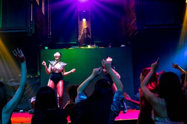 Bir grup insan disko gece kulübünde DJ 'in sahnede çaldığı müzikle dans ediyor.