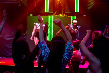 Bir grup insan disko gece kulübünde DJ 'in sahnede çaldığı müzikle dans ediyor.
