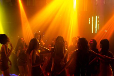 Disko gece kulübünde DJ 'in sahnede yaptığı müzikle dans eden insanların silueti.