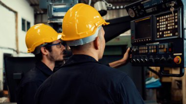 Bir grup yetenekli fabrika işçisi atölyede makine ekipmanı kullanıyor.