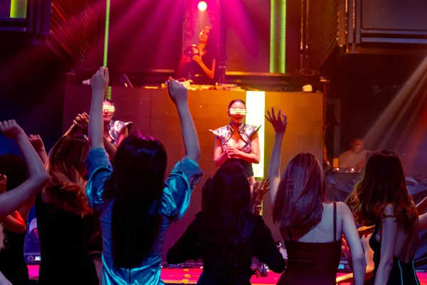 Grupo de personas bailan en discoteca al ritmo de la música de DJ en el escenario — Foto de Stock