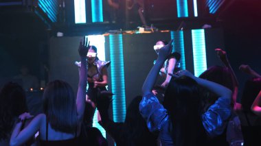 Bir grup insan disko gece kulübünde DJ 'in sahnede çaldığı müzikle dans ediyor.