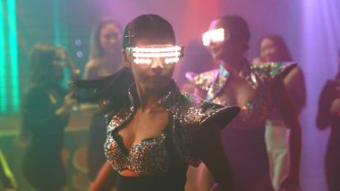 Bir grup insan disko gece kulübünde DJ 'in sahnede çaldığı müzikle dans ediyor.