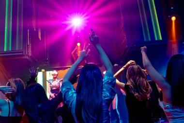 Bir grup insan disko gece kulübünde DJ 'in sahnede çaldığı müzikle dans ediyor.