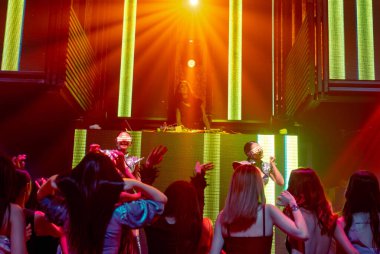 Bir grup insan disko gece kulübünde DJ 'in sahnede çaldığı müzikle dans ediyor.