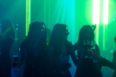 Disko gece kulübünde DJ 'in sahnede yaptığı müzikle dans eden insanların silueti.