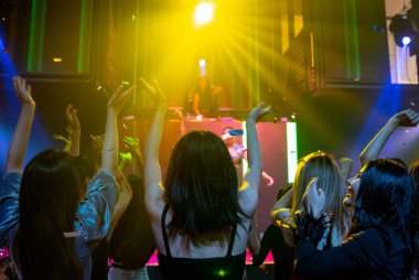 Bir grup insan disko gece kulübünde DJ 'in sahnede çaldığı müzikle dans ediyor.