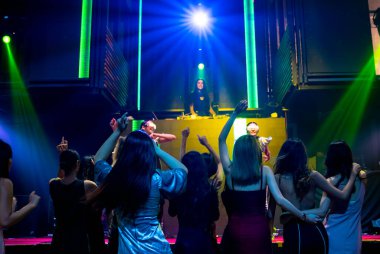 Bir grup insan disko gece kulübünde DJ 'in sahnede çaldığı müzikle dans ediyor.