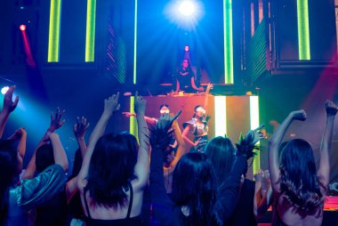 Bir grup insan disko gece kulübünde DJ 'in sahnede çaldığı müzikle dans ediyor.
