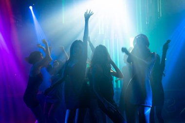 Disko gece kulübünde DJ 'in sahnede yaptığı müzikle dans eden insanların silueti.