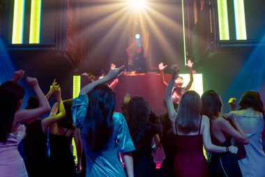 Bir grup insan disko gece kulübünde DJ 'in sahnede çaldığı müzikle dans ediyor.