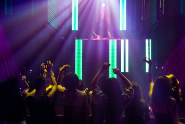 Disko gece kulübünde DJ 'in sahnede yaptığı müzikle dans eden insanların silueti.