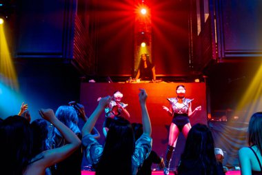 Bir grup insan disko gece kulübünde DJ 'in sahnede çaldığı müzikle dans ediyor.