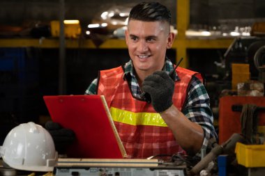 Fabrika işçisi, makine parçalarını incelerken taşınabilir radyodan konuşuyor.