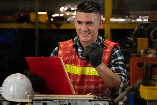 Fabrika işçisi, makine parçalarını incelerken taşınabilir radyodan konuşuyor.