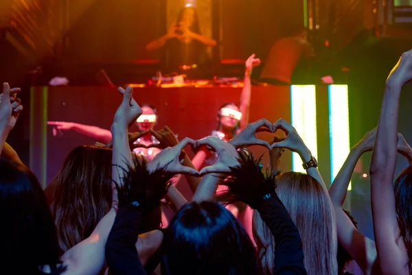 Grupp av människor dansar i disco nattklubb till rytmen av musik från DJ på scenen — Stockfoto