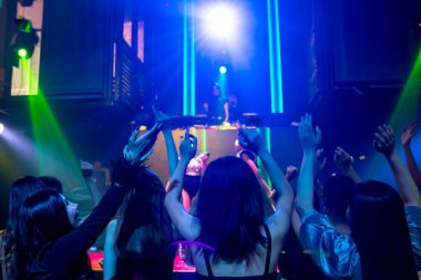 Bir grup insan disko gece kulübünde DJ 'in sahnede çaldığı müzikle dans ediyor.