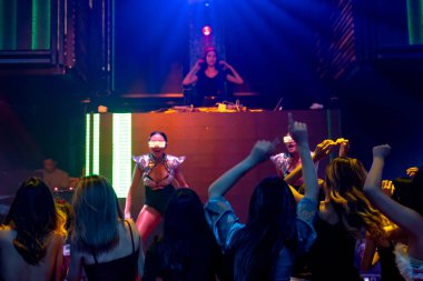 Bir grup insan disko gece kulübünde DJ 'in sahnede çaldığı müzikle dans ediyor.