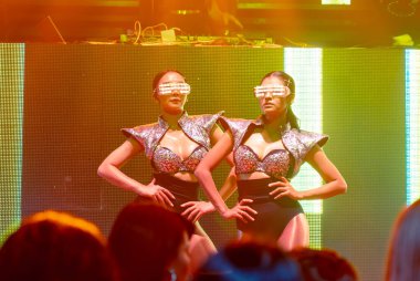 Bir grup insan disko gece kulübünde DJ 'in sahnede çaldığı müzikle dans ediyor.