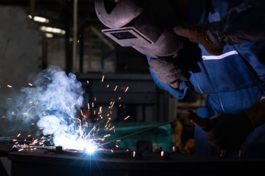 Fabrikada kaynak makinesiyle çalışan yetenekli bir metal işçisi.