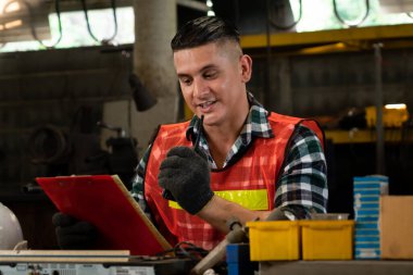 Fabrika işçisi, makine parçalarını incelerken taşınabilir radyodan konuşuyor.