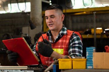 Fabrika işçisi, makine parçalarını incelerken taşınabilir radyodan konuşuyor.
