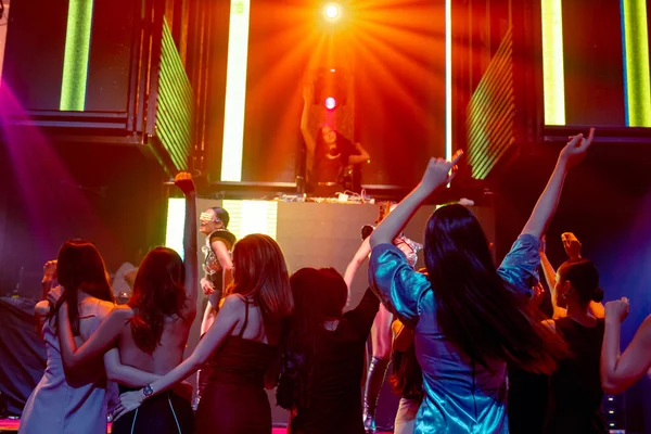 Group of people dance in disco night club to the beat of music from DJ on stage