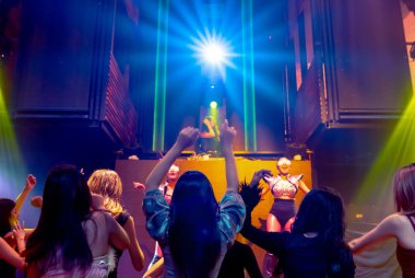 Bir grup insan disko gece kulübünde DJ 'in sahnede çaldığı müzikle dans ediyor.