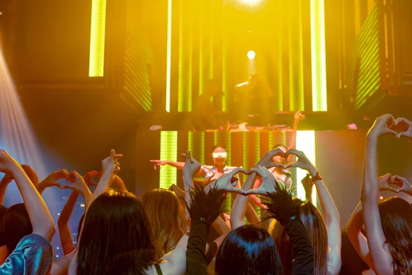 Grupp av människor dansar i disco nattklubb till rytmen av musik från DJ på scenen — Stockfoto