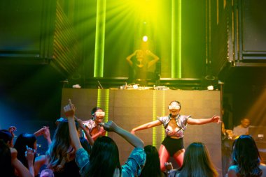 Bir grup insan disko gece kulübünde DJ 'in sahnede çaldığı müzikle dans ediyor.