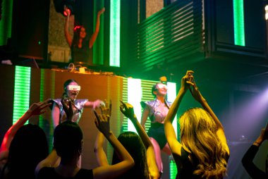Bir grup insan disko gece kulübünde DJ 'in sahnede çaldığı müzikle dans ediyor.