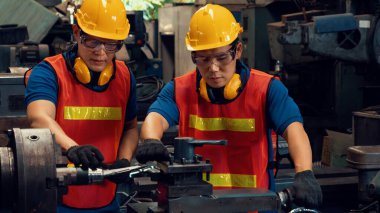 Bir grup yetenekli fabrika işçisi atölyede makine ekipmanı kullanıyor.