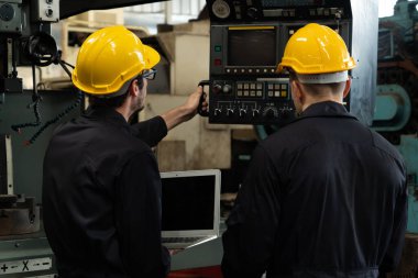 Bir grup yetenekli fabrika işçisi atölyede makine ekipmanı kullanıyor.