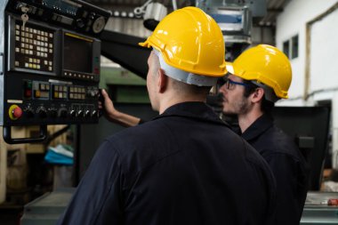 Bir grup yetenekli fabrika işçisi atölyede makine ekipmanı kullanıyor.