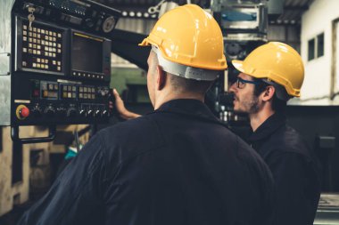 Bir grup yetenekli fabrika işçisi atölyede makine ekipmanı kullanıyor.