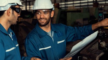 Bir grup yetenekli fabrika işçisi atölyede makine ekipmanı kullanıyor.