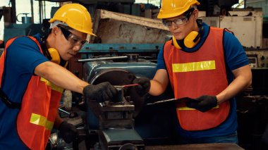 Bir grup yetenekli fabrika işçisi atölyede makine ekipmanı kullanıyor.