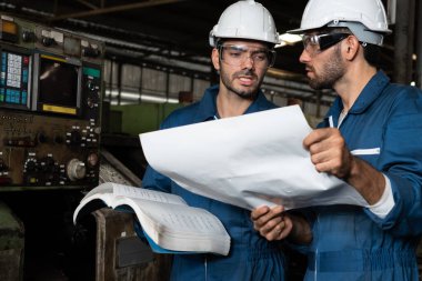 Bir grup yetenekli fabrika işçisi atölyede makine ekipmanı kullanıyor.