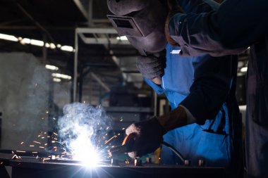 Fabrikada kaynak makinesiyle çalışan yetenekli bir metal işçisi.