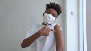 Afro-Amerikalı genç COVID-19 aşısını neşeyle gösteriyor.