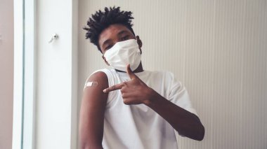 Afro-Amerikalı genç COVID-19 aşısını neşeyle gösteriyor.