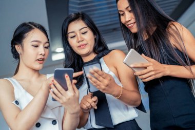 Üç kadın arkadaş cep telefonu aygıtıyla konuşuyor.