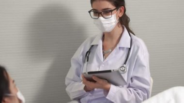 Yüz maskesi takan doktor hastane koğuşundaki hastalarla düzgün bir şekilde konuşuyor.