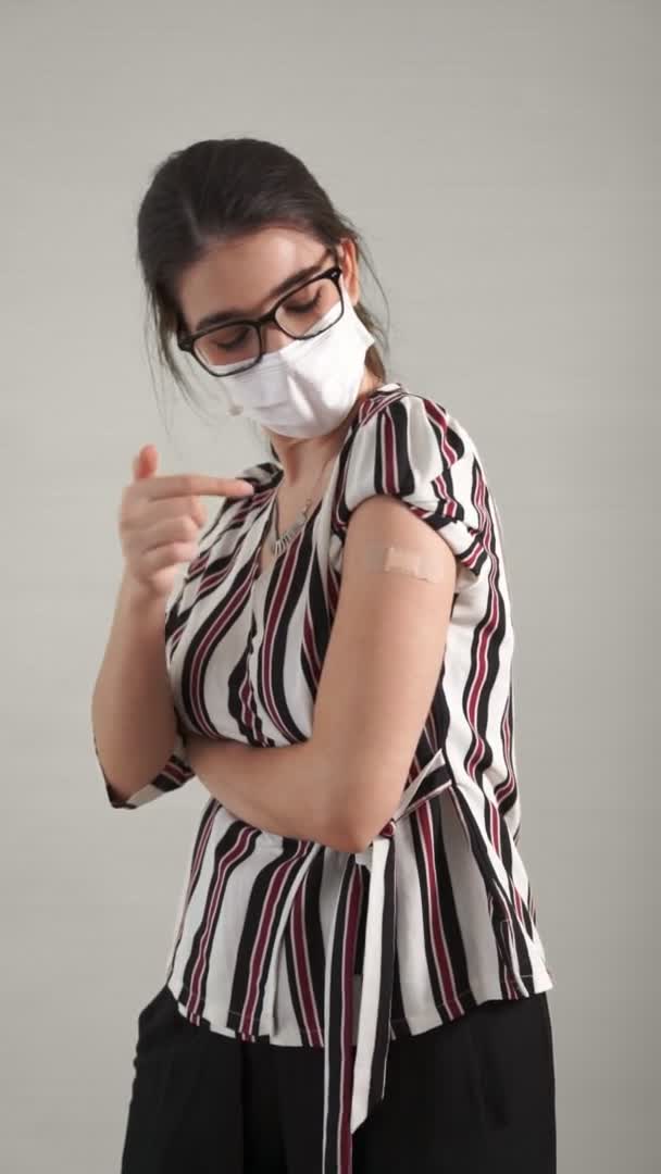 Vídeo vertical de una mujer joven mostrando alegremente el vendaje de la vacuna COVID-19 — Vídeos de Stock