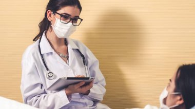 Yüz maskesi takan doktor hastane koğuşundaki hastalarla düzgün bir şekilde konuşuyor.