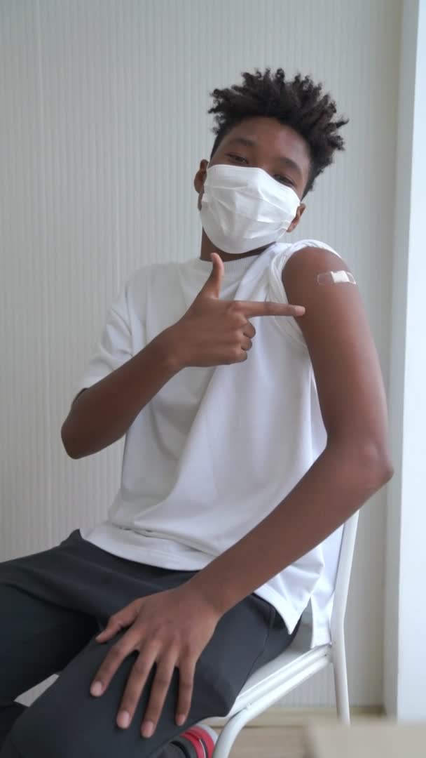 Вертикальное видео африканского подростка, весело показывающего повязку от вакцины COVID-19 — стоковое видео