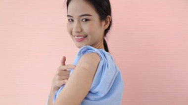 Genç Asyalı kadın COVID-19 aşısını neşeyle gösteriyor.