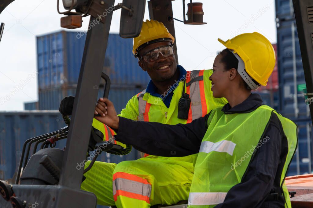African american man and woman driving forklift in shipyard .