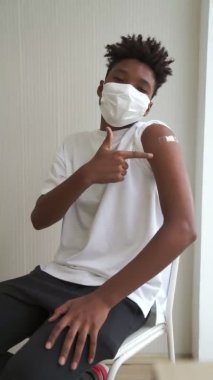 Afrikalı bir gencin dikey videosu COVID-19 aşı bandajını neşeyle gösteriyor.