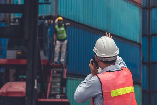 Industrial worker works with co-worker at overseas shipping container yard